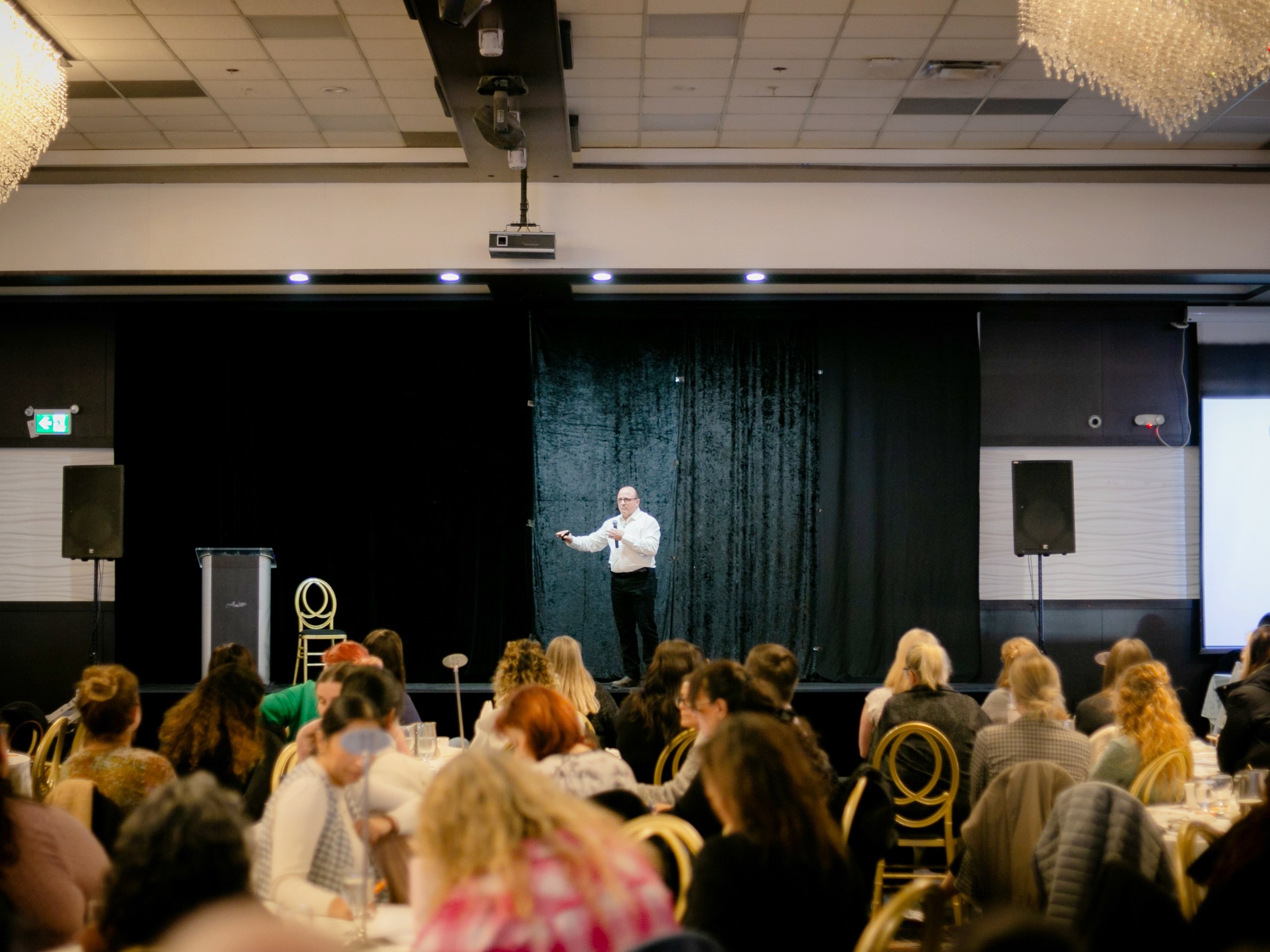 Trace Hobson presenting on stage to a leadership audience, gesturing to illustrate where capacity comes from
